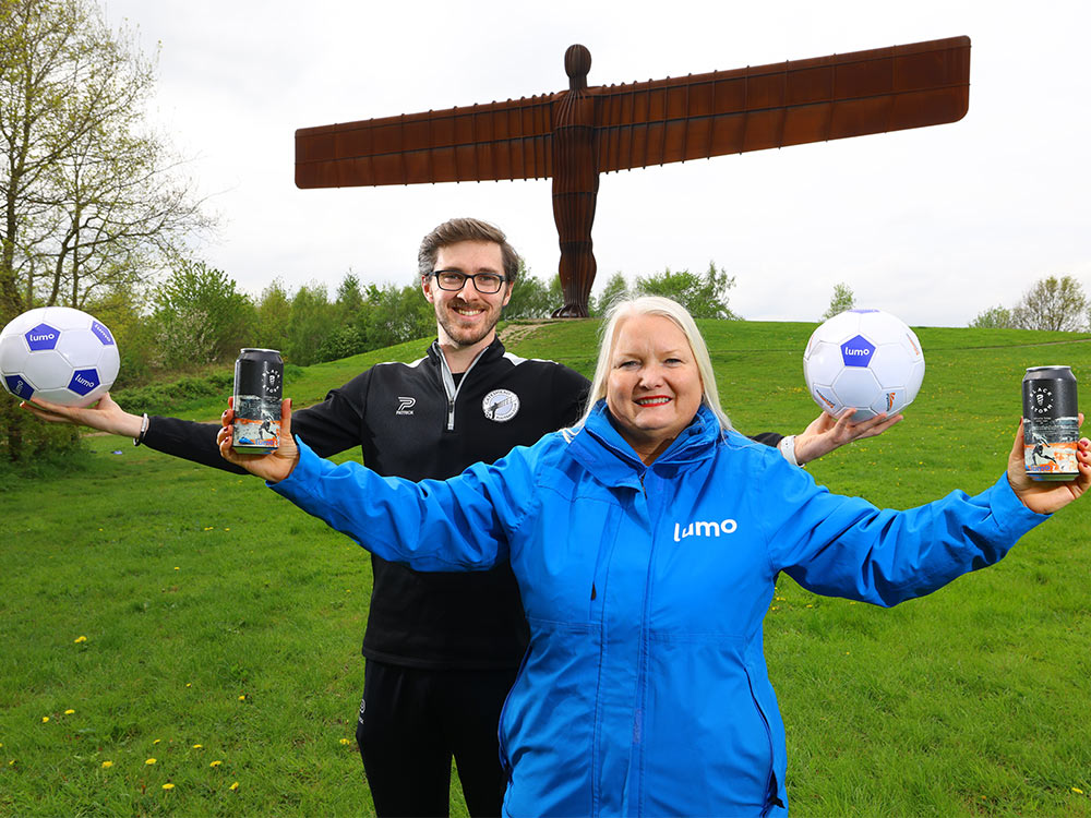 Lumo and Gateshead FC staff members holding cans of the new beer in front of Angel of the North