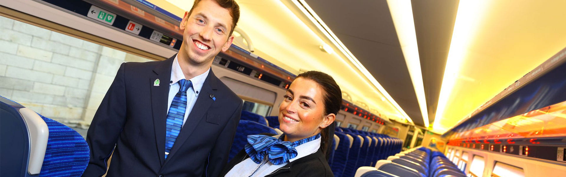 Two Lumo staff members in the new uniforms standing on the aisle of the train